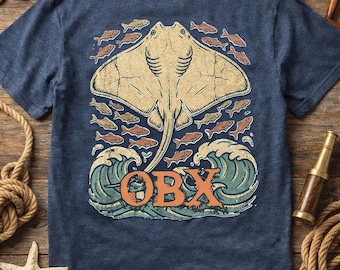 May include: A navy blue t-shirt featuring a large, distressed-style graphic on the back. The design depicts a tan stingray swimming above stylized teal ocean waves, surrounded by small orange fish. The text OBX is printed in orange.