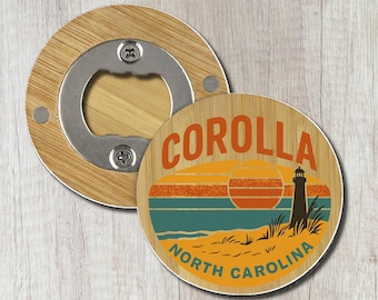 May include: A round wooden bottle opener featuring a graphic of a lighthouse on a beach at sunset. The text COROLLA and NORTH CAROLINA is printed in orange. The metal opener mechanism is visible on the top portion of the circular wooden base.