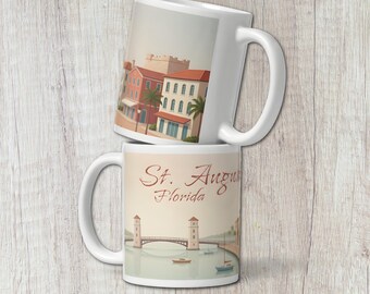 May include: A white ceramic mug featuring a graphic illustration of St. Augustine, Florida, with a bridge, boats, and coastal buildings. The text St. Augustine Florida is printed in a brown script font above the bridge and water scene.