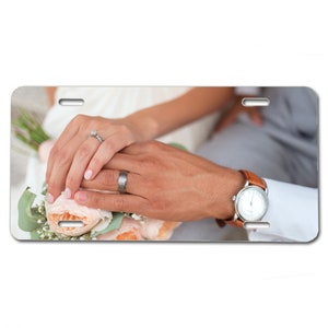 May include: A close-up of a couple's hands with wedding rings on their fingers. The bride is holding a bouquet of white and peach flowers. The groom is wearing a brown leather watch.