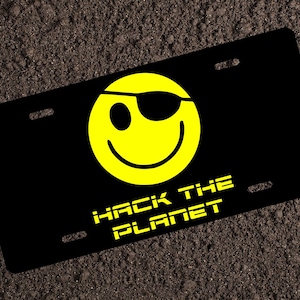 May include: Black license plate with a yellow smiley face with an eye patch and the text "Hack the Planet" in yellow.