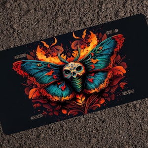 May include: A colorful, skull-like moth with blue, orange, and yellow wings. The moth is surrounded by red and orange floral designs on a black background.