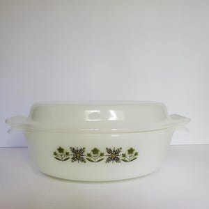 May include: A white oval casserole dish with a matching lid. The dish features a decorative floral pattern in green and brown. The dish has two handles and is suitable for baking and serving.