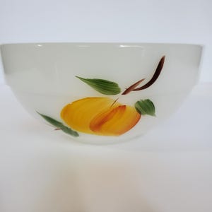 May include: White ceramic bowl with a hand-painted design of a yellow and orange fruit with green leaves and brown stems. The bowl has a wide, rounded shape.