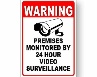 Pode incluir: Um sinal branco com borda vermelha e texto preto que diz "WARNING" em letras grandes. Abaixo do aviso, há uma imagem em preto e branco de uma câmera de segurança. O texto abaixo da imagem diz "PREMISES MONITORED BY 24 HOUR VIDEO SURVEILLANCE".