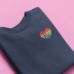 Pu&ograve; includere: Una felpa blu navy con un design a forma di cuore arcobaleno con la parola "Love" all'interno.