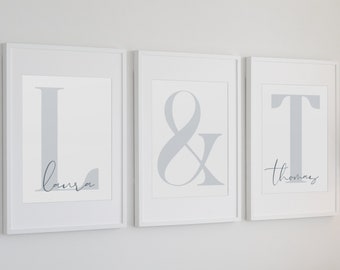 May include: Three framed prints with gray letters and ampersand symbol. The first print has the letter L and the name Laura. The second print has the ampersand symbol. The third print has the letter T and the name Thomas.
