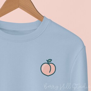 May include: A light blue sweatshirt with a peach graphic and the text "Peachy" on the front.