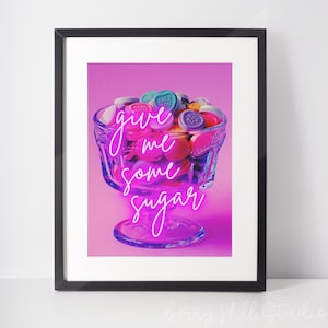 Puede incluir: Un tazón de vidrio lleno de corazones de caramelo coloridos con frases como "Cool Girl", "Only You" y "Hug Me". El tazón está sobre un fondo rosa con el texto rosa neón "give me some sugar".