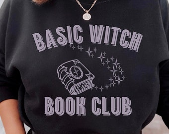Puede incluir: Una sudadera negra con el texto "Basic Witch Book Club" en color morado claro. El texto está en una fuente de estilo vintage. Una imagen estilizada de un libro con estrellas alrededor está encima del texto.