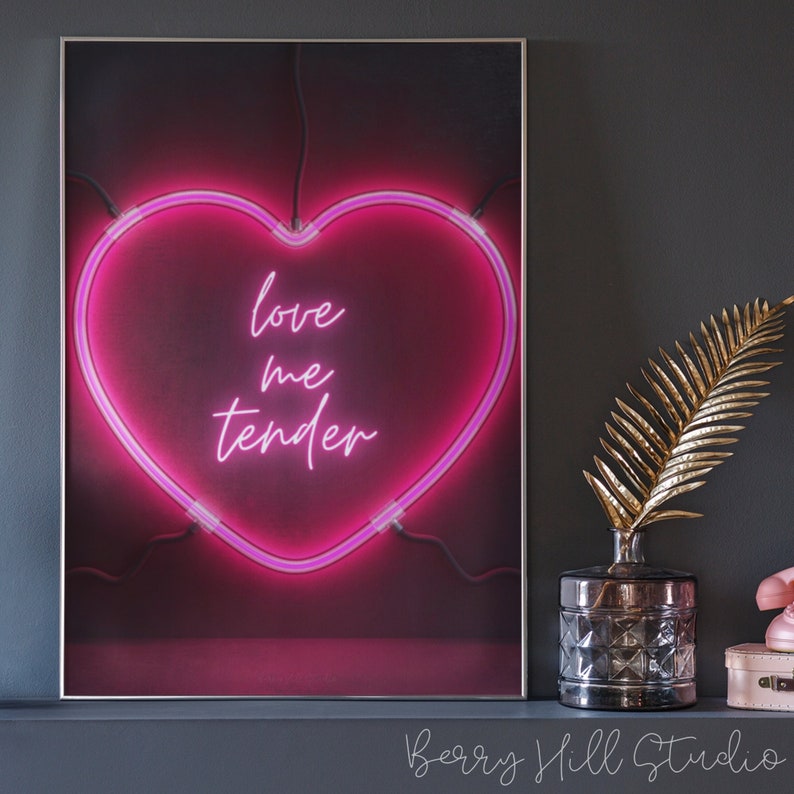May include: A pink neon heart-shaped sign with the text "love me tender" on a dark background.