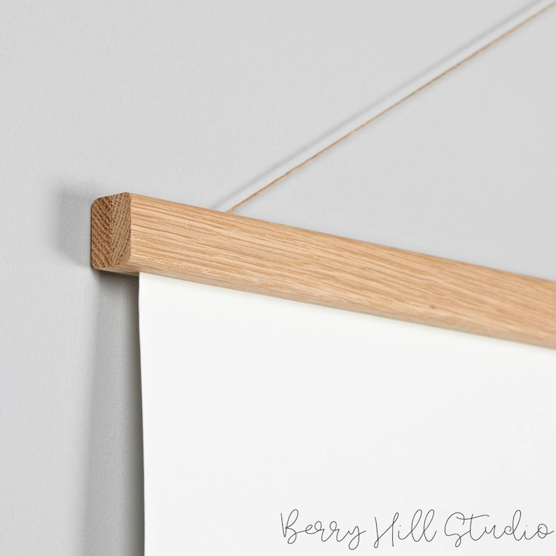 May include: A close-up of a natural wood poster hanger with a string attached. The hanger is designed to hold a poster or artwork.