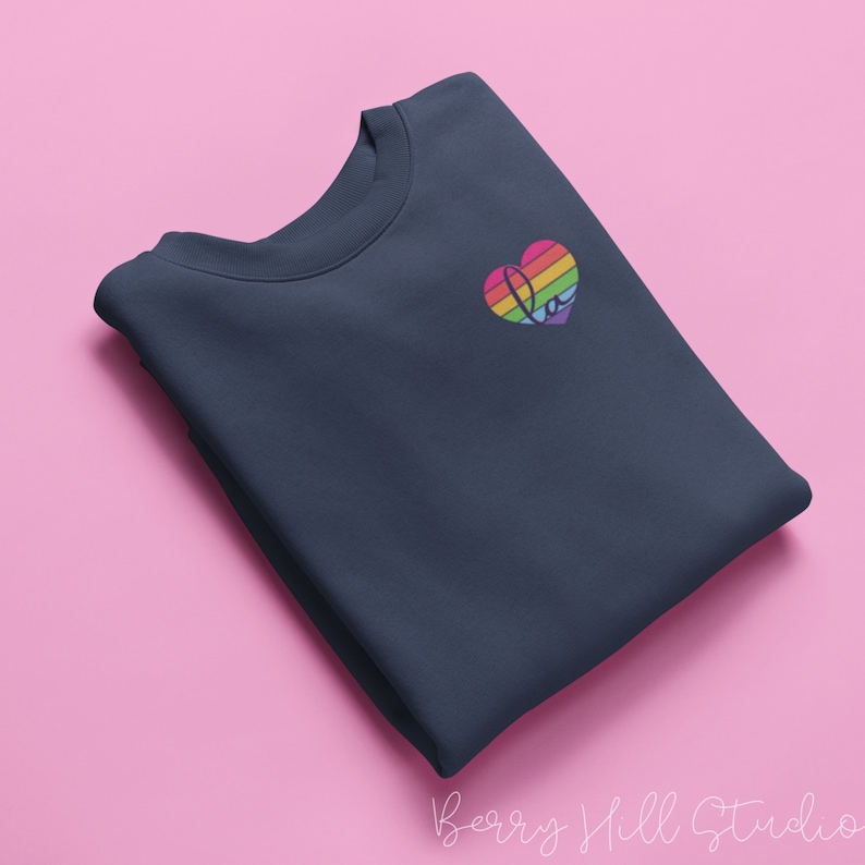 Pu&ograve; includere: Una felpa blu navy con un design a forma di cuore arcobaleno con la parola "Love" all'interno.