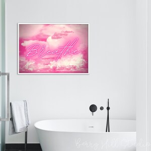 May include: A pink and white abstract art print with the word "Breathe" in neon pink lettering. The print is framed in a white frame and is hanging on a white wall.