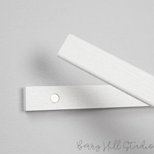 May include: Two white wooden strips with a metal circle attached to one of the strips. The strips are used to hang items on a wall.