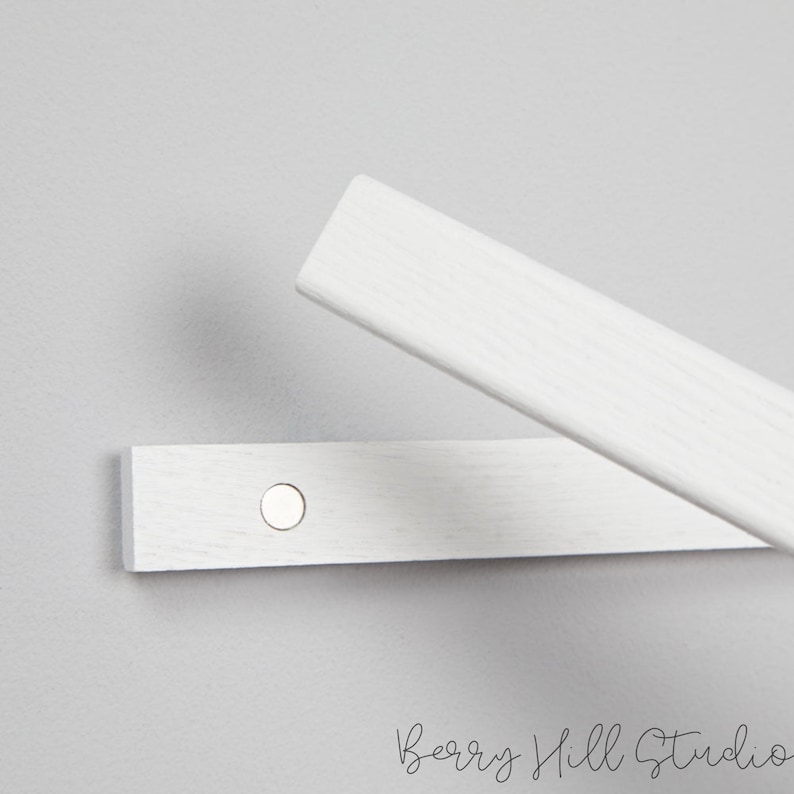 May include: Two white wooden strips with a metal circle attached to one of the strips. The strips are used to hang items on a wall.