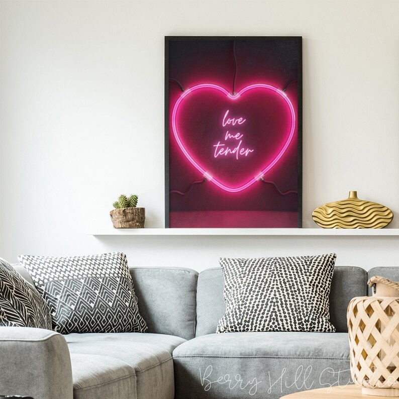 May include: A black framed print with a pink neon heart that says "love me tender" on a red background.