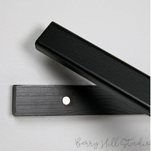 May include: Black wooden shelf brackets with a silver screw in the center. The brackets are designed to be mounted to a wall.