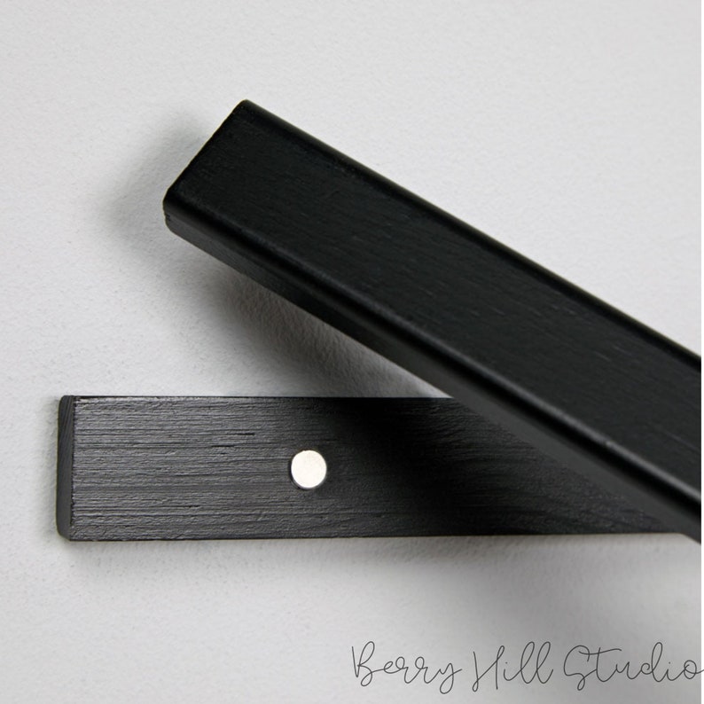 May include: Black wooden shelf brackets with a silver screw in the center. The brackets are designed to be mounted to a wall.
