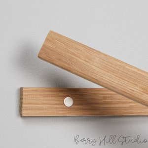 May include: Two wooden strips with a silver magnetic button connecting them. The strips are light brown and have a wood grain pattern.