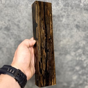 Puede incluir: Un bloque de madera marrón oscuro y negro con un patrón de veta único. La madera es lisa y pulida.