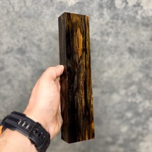 May include: A dark brown and gold wood block with a unique grain pattern. The block is approximately 5 inches long and 1.5 inches wide.