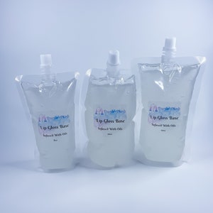 May include: Three clear plastic pouches filled with a clear liquid, each with a white spout and a label that reads "Lip Gloss Base Infused With Oils." The pouches are labeled 8oz, 10oz, and 12oz. The brand name "Purple Plush" is also visible.