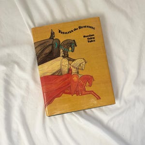 Puede incluir: Un libro antiguo titulado "Vasilisa la Bella" con ilustraciones de jinetes a caballo. La portada es de color amarillo mostaza con el título en negro y las palabras "Cuentos de hadas rusos".