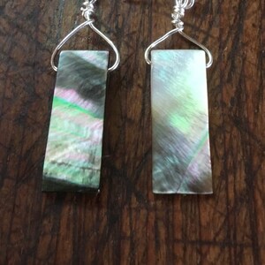 Può includere: Un paio di orecchini d'argento con pendenti rettangolari in madreperla di abalone verde e nero iridescente.