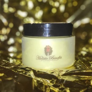 Op de afbeelding: Een witte pot met een zwarte deksel en een gouden kroonlogo. De pot is gelabeld met "Holistic Benefits" in een cursief schrift. De pot staat op een gouden achtergrond.