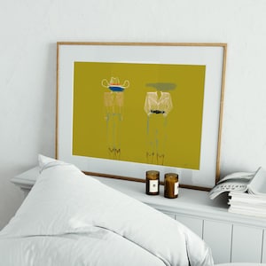 May include: Abstract art print with two figures on a mustard-yellow background, framed in light wood. One figure wears a cowboy hat, the other a hat with a green smudge. The artwork is displayed on a white dresser with candles and a pillow.