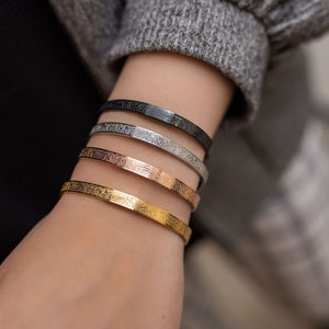May include: Four gold, silver, and black bangle bracelets with intricate Arabic calligraphy designs.