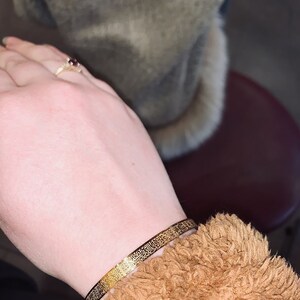 May include: A gold bracelet with intricate Arabic calligraphy etched into the metal.