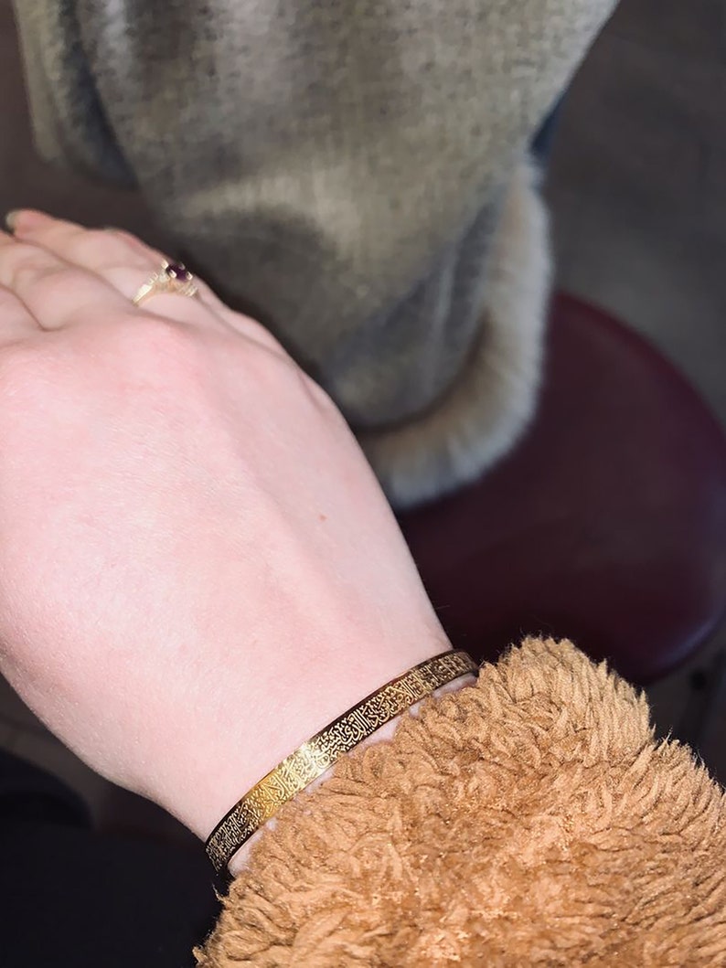 May include: A gold bracelet with intricate Arabic calligraphy etched into the metal.
