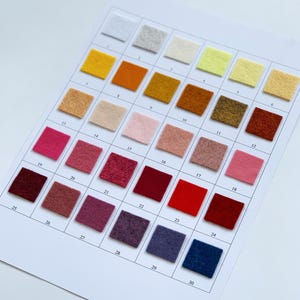 May include: A color chart featuring 30 small, square felt swatches in a variety of colors, including white, yellow, orange, brown, pink, red, and blue. The swatches are arranged in a grid and numbered for easy reference. The chart is on a white background.