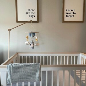 May include: A baby crib with a light blue blanket and a mobile featuring clouds, stars, and an elephant. Two framed prints above the crib read "these are the days" and "i never want to forget".