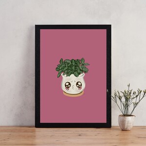 May include: A framed print of a cartoon illustration of a potted plant with a cute face. The plant is in a white pot with a pink background. The frame is black.