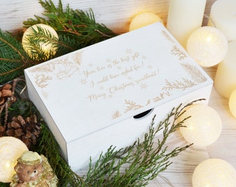 May include: A white wooden box with a decorative design and the text "Your love is the best gift I could have asked for! Merry Christmas sweetheart!" is surrounded by greenery, candles, and string lights.