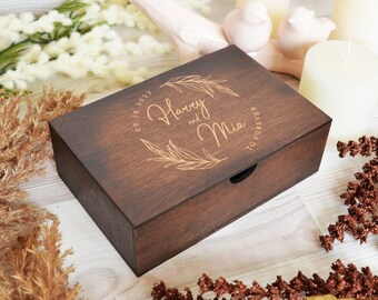 Puede incluir: Una caja de madera marrón oscuro con una tapa deslizante. La caja está grabada con el texto "Harry y Mia" y la fecha "09.18.2022" en una fuente dorada. El texto "Para siempre" también está grabado en la caja.