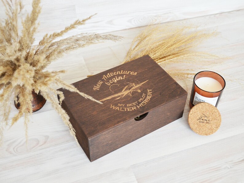 May include: A dark brown wooden box with a hinged lid and a pull-out drawer. The box is engraved with the text "New Adventures begin!" and a small airplane. Below the airplane is the text "My Best Pilot Walter Herbert".