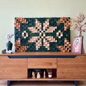 Puede incluir: Una pieza de arte de pared de madera con un diseño geométrico en tonos verdes y marrones. El arte está montado en una pared sobre un gabinete de madera con acentos negros.