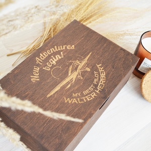 May include: A dark brown wooden box with an engraved design of a plane and the text "New Adventures begin! My Best Pilot Walter Herbert".