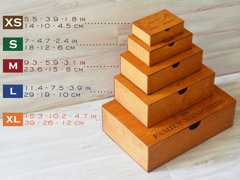 May include: Set of five wooden boxes with lids, ranging in size from extra small to extra large. The boxes are stacked on top of each other, with the largest box at the bottom. The boxes are all made of natural wood and have a light brown finish. The lids of the boxes are engraved with the words "Family Memories". The boxes are labeled with their size and dimensions in inches and centimeters.