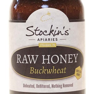 May include: A glass jar of Stockin's Apiaries raw buckwheat honey. The label is brown with white text that reads "Stockin's Apiaries, Strasburg, PA, Raw Honey, Buckwheat, Unheated, Unfiltered, Nothing Removed, Net Wt. 10 oz. (283 g)". A small yellow hexagon with the text "100% USA Honey" is in the upper right corner of the label.