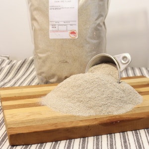 May include: A large bag of dark rye flour with a scoop of flour on a wooden cutting board. The bag has a label that says "Dark Rye Flour".