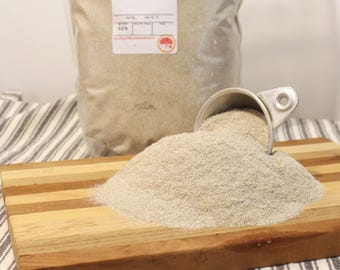 May include: A large bag of dark rye flour with a scoop of flour on a wooden cutting board. The bag has a label that says "Dark Rye Flour".