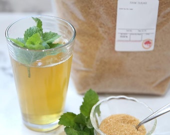 May include: A glass of iced tea with fresh mint leaves, a small bowl of brown sugar, and a bag of raw sugar.
