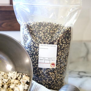 May include: A clear plastic bag filled with non-GMO blue popcorn kernels. The bag has a label that reads "Non-GMO Blue Popcorn".