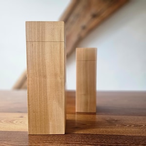 Op de afbeelding: Twee houten dozen met deksels. De dozen zijn rechthoekig en gemaakt van lichtgekleurd hout. De grotere doos staat op de voorgrond en de kleinere doos erachter. De dozen staan op een houten oppervlak.