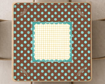 May include: A square table cover featuring a brown background with a repeating pattern of light blue polka dots. The centre displays a white and yellow checkered square framed by a scalloped light blue border with small white text along the edges.